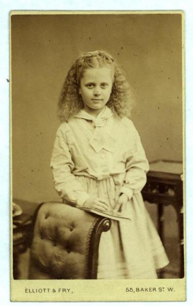 Ritratto infantile - Bambina in piedi, appoggiata allo schienale imbottito di una poltroncina