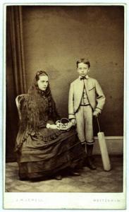 Ritratto di famiglia (?) - Giovane donna seduta su una sedia accanto a un bambino in piedi, con la mazza da cricket a fianco