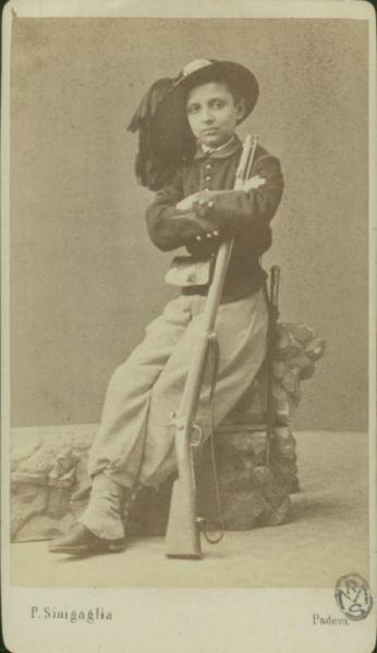 Ritratto maschile - Giovane in abito da bersagliere con un fucile in mano, seduto su un masso finto a braccia conserte