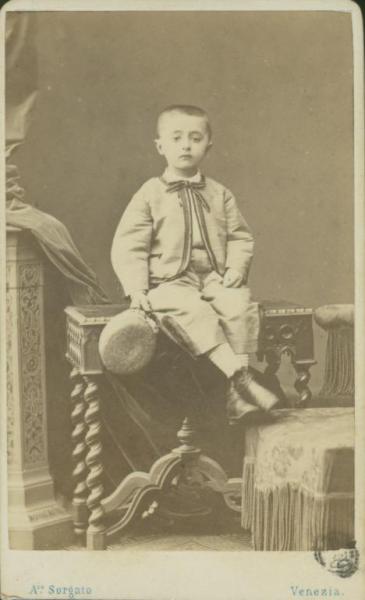 Ritratto infantile - Bambino seduto su una consolle con i piedi appoggiati su uno sgabello