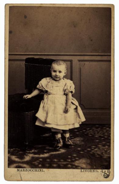Ritratto infantile - Bambina in piedi appoggiata a una poltroncina