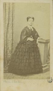 Ritratto femminile - Donna in abito scuro con con un fiore in mano, in piedi appoggiata ad un piedistallo