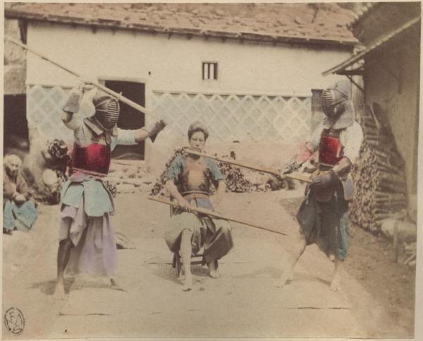 Giappone - Cortile - Due uomini si affrontano in un'esercitazione di kendo con i bastoni - Un arbitro al centro - Un anziano guarda la scena seduto sulla sinistra