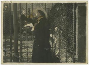 Ritratto femminile - Donna, attrice, con cappello appoggiata alla rete di un cancello - Esterno
