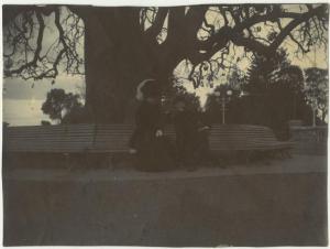 Esterno, mare - Ritratto di coppia - Elvira Lazzaroni con uomo seduti su una panchina - Albero - Ombra di Leopoldo Metlicovitz