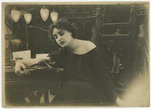 Set cinematografico, interno - Ritratto femminile - Pina Menichelli, attrice, seduta davanti a tavolo con crocifisso