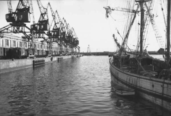Viaggio verso l'Africa. Napoli: imbarcazione ormeggiata in porto e scorcio del molo con i magazzini e le gru