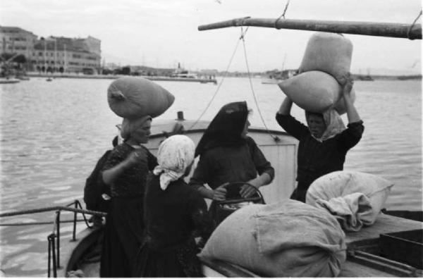 Viaggio in Jugoslavia. Sebenico: un gruppo di contadine carica la merce appena acquistata sulle proprie imbarcazioni