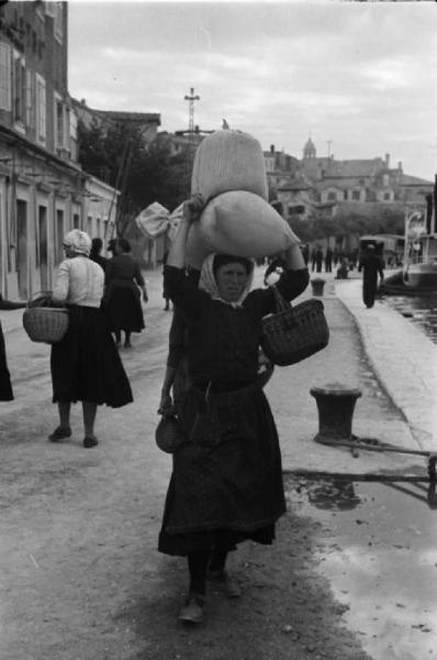 Viaggio in Jugoslavia. Sebenico: un gruppo di donne porta la merce appena acquistata al mercato verso le proprie imbarcazioni