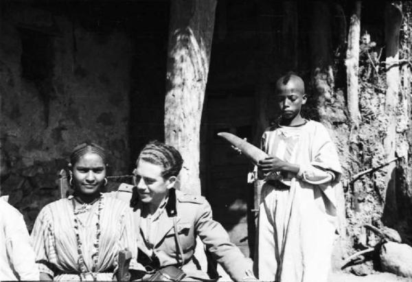 Viaggio in Africa. Insediamento indigeno di Mai Otza - soldato italiano seduto si riposa - al suo fianco alcuni indigeni