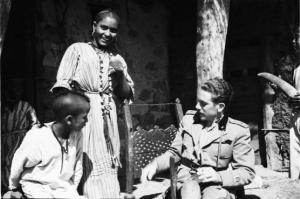 Viaggio in Africa. Insediamento indigeno di Mai Otza - soldato italiano seduto si riposa - al suo fianco alcuni indigeni