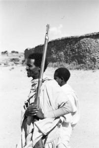 Viaggio in Africa. Un indigeno fa la guardia reggendo un fucile, accanto a lui un ragazzino