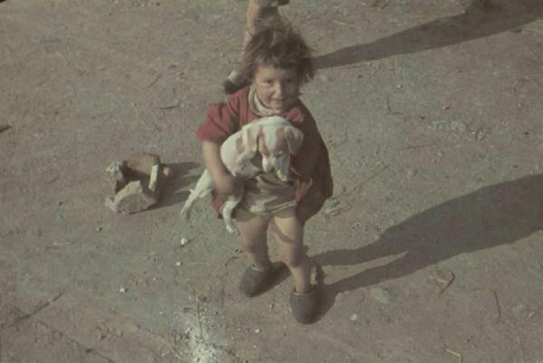 Periferia di Milano: campo nomadi. Ritratto femminile, bambina che tiene in braccio un cucciolo di cane