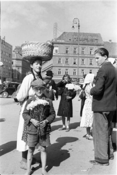 Viaggio in Jugoslavia. Zagabria: mercato. Ritratto di gruppo, donna croata con cesta in testa, bambino con mazzo di fiori e passante che li osserva