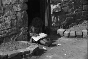 Periferia di Milano: bambina zingara seduta sulla soglia di una baracca