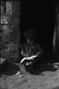 Periferia di Milano: bambina zingara seduta sulla soglia di una baracca