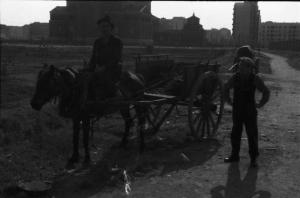 Periferia di Milano: ritratto di maschile, uomo a cavallo che traina un carretto lungo una via sterrata a ridosso della città