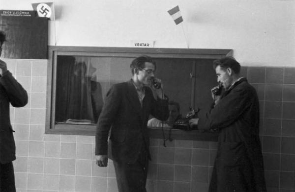 Viaggio in Jugoslavia. Ospedale di Zagabria: due uomini che parlano al telefono. Accanto una bacheca che reca la svastica nazista