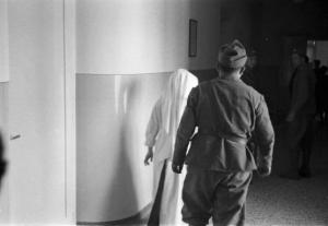 Viaggio in Jugoslavia. Ospedale di Zagabria: una suora e un soldato ripresi da tergo mentre camminano in un corridoio