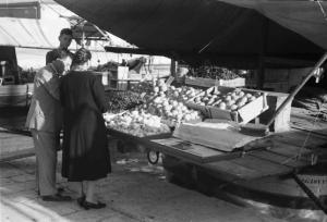 Viaggio in Jugoslavia. Sebenico: coppia di persone al mercato, davanti a una bancarella della frutta