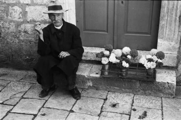 Viaggio in Jugoslavia. Dubrovnik (Ragusa): un anziano venditore di fiori seduto sopra un gradino