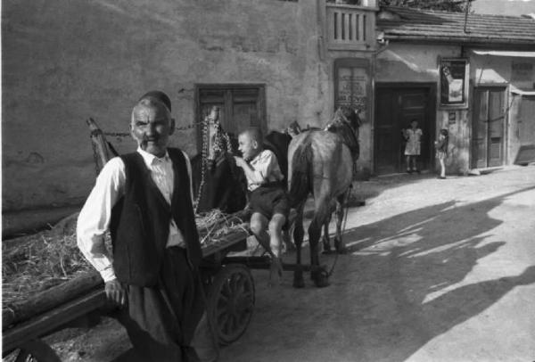 Viaggio in Jugoslavia. Mostar: scorcio di una via, in primo piano un uomo si appoggia a un carro trainato da cavalli