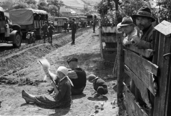Campagna di Russia. Bessarabia - Riscani - abitanti osservano il passaggio della colonna di automezzi militari - donna lavora la lana al fuso - bambino gioca con pulcini
