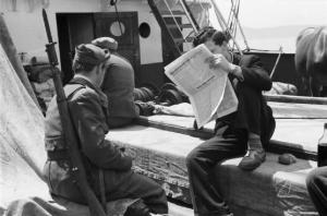 Viaggio in Jugoslavia. Verso Dubrovnik (Ragusa):  scorcio della coperta dell'imbarcazione - si riconosce un militare Ustascia di spalle e un viaggiatore assorto nella lettura di un giornale