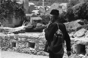 Viaggio in Jugoslavia. Mostar: scene di vita quotidiana - uomo anziano con zaino in spalla percorre una strada del paese visibile sullo sfondo