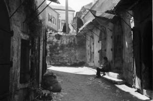 Viaggio in Jugoslavia. Mostar: scene di vita quotidiana - scorcio del paese con uomo seduto sulla soglia di un'abitazione
