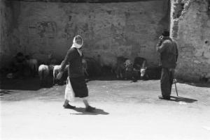 Viaggio in Jugoslavia. Mostar: donna cammina lungo una strada; alle spalle un pastore con i suoi animali