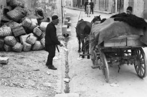Viaggio in Jugoslavia. Mostar: scene di vita quotidiana - carro trainato da cavalli in sosta lungo una strada del paese. Sulla sinistra è visibile una catasta di ceste
