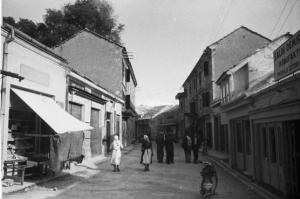 Viaggio in Jugoslavia. Mostar: scene di vita quotidiana - gruppo di abitanti percorre una strada in cui si trovano alcuni negozi