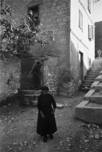 Viaggio in Jugoslavia. Mostar: scorcio della città - una donna anziana in primo piano attraversa uno slargo mentre alle sue spalle una coppia di uomini discute