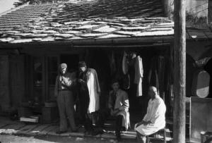 Viaggio in Jugoslavia. Mostar: scene di vita quotidiana - gruppo di uomini sulla soglia di un negozio di abbigliamento