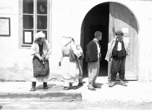 Viaggio in Jugoslavia. Yaitze: due coppie di donne e uomini in costume locale sostano nei pressi del portone d'ingresso di un palazzo