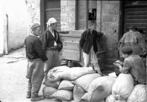 Viaggio in Jugoslavia. Yaitze: gruppo di abitanti sosta nei pressi di un magazzino di fianco a un cumulo di sacchi