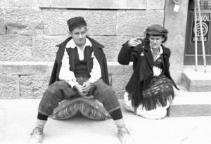 Viaggio in Jugoslavia. Yaitze: coppia di giovani abitanti in costume locale seduta su un marciapiede, nei pressi della zona del mercato