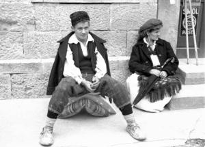 Viaggio in Jugoslavia. Yaitze: coppia di giovani abitanti in costume locale seduta sopra un marciapiede, nella zona del mercato