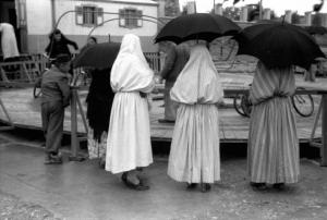 Viaggio in Jugoslavia. Banja Luka: scorcio nella zona del mercato nei pressi della giostra - in primo piano tre donne bosniache in abito locale sorprese di spalle sotto un ombrello