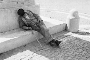 Roma - isola Tiberina. Anziano senzatetto si riposa all'ombra di un obelisco nella piazza di Santa Maria in Trastevere