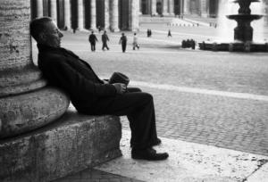 Roma. Scorcio di Piazza San Pietro. In primo piano un uomo anziano si riposa seduto ai piedi di una colonna