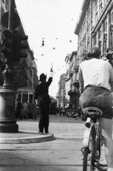 Italia Dopoguerra. Milano - Piazza del Duomo - vigile dirige il traffico - In primo piano un giovane in bicicletta