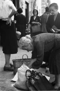 Italia Dopoguerra. Savona - Anziana donna china sulle borse della spesa