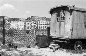 Italia Dopoguerra. Milano - Periferia - Baracche - Carrozzone adibito ad abitazione addossato ad un muro di mattoni riportante alcune scritte