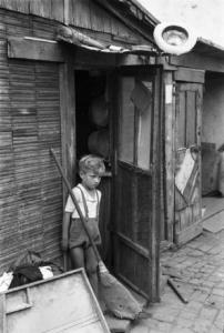 Italia Dopoguerra. Milano - Periferia - Baraccopoli - Bambino sulla soglia di una baracca