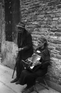 Italia Dopoguerra. Milano - Coppia di anziani mendicanti - la donna suona la fisarmonica mentre l'uomo chiede l'elemosina