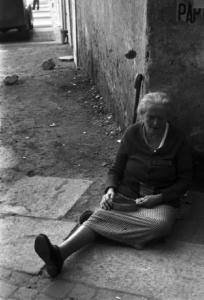 Italia Dopoguerra. Milano - Donna anziana seduta per strada chiede l'elemosina