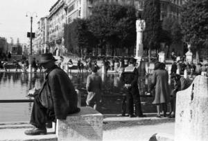 Roma. Gente a passeggio nei pressi di una fontana recante simboli del regime fascista - in primo piano un uomo seduto su un gradino di marmo
