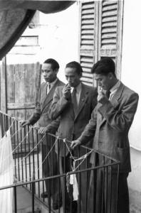 Italia Dopoguerra. Milano - Quartiere cinese - tre cinesi con espressioni serie fumano una sigaretta sul ballatoio di una casa a ringhiera